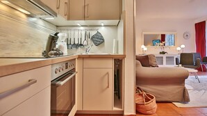 A compact kitchen with modern appliances, a dining area with a sofa and chairs, and a living room with a TV and decorative items. - Haus Parkblick Apartment 10 - Haus Parkblick, Timmendorfer Strand (Timmendorfer Strand)