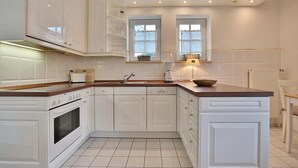 Une cuisine avec des meubles blancs, un plan de travail en bois, un four encastré et une fenêtre au-dessus de l’évier.