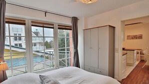 Une chambre avec un grand lit, une armoire et une vue sur une piscine par la fenêtre.