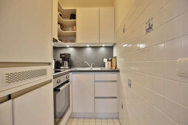 A compact kitchen with white cabinets, a built-in oven, a coffee maker, and a sink. - Carpe Diem Appartement 093 - Carpe Diem (Timmendorfer Strand)