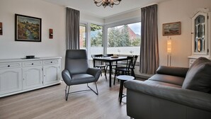 A modern living room with a dining area, featuring a chandelier, leather furniture, and large windows with curtains. - Carpe Diem Appartement 093 - Carpe Diem (Timmendorfer Strand)