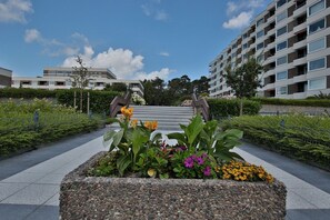 A modern building with a central staircase, surrounded by landscaped areas with various plants and flowers.