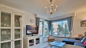 A living room with a television, a chandelier, a sofa, and a window with curtains. - Carpe Diem Apartment 109 - Carpe Diem (Timmendorfer Strand)