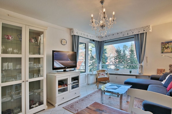 A living room with a television, a chandelier, a sofa, and a window with curtains.
