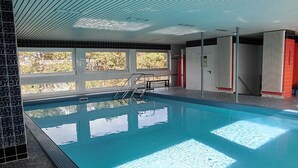 An indoor swimming pool with clear blue water, a ladder, and a view of trees outside. - Carpe Diem Apartment 109 - Carpe Diem (Timmendorfer Strand)
