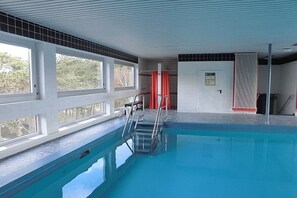 An indoor swimming pool with clear windows, a lifeguard chair, and a safety sign on the wall.