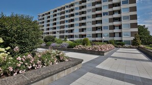 A modern multi-story residential building with a uniform facade, balconies, and a landscaped courtyard with flower beds. - Carpe Diem Apartment 109 - Carpe Diem (Timmendorfer Strand)