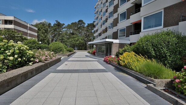 A modern building with a central courtyard, surrounded by greenery and flower beds. - Carpe Diem Apartment 109 - Carpe Diem (Timmendorfer Strand)