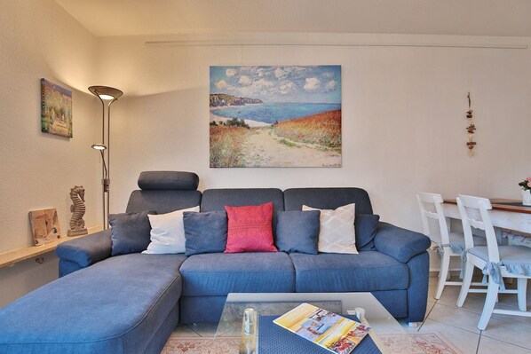 A living room with a grey sofa, a coffee table, and a painting of a coastal landscape.