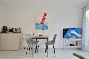 En moderne stue med spiseplads, et maleri af en sejlbåd, et fladskærms-tv og et tekøkken.
