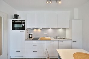 Una cocina moderna con gabinetes blancos, horno empotrado, cafetera y lavaplatos.