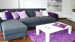 Una sala moderna con un sofá seccional gris, una mesa de centro blanca y una alfombra mullida color púrpura.
