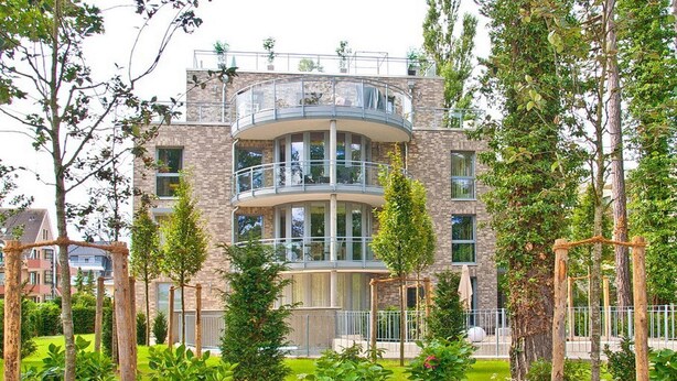 Un edificio residencial de varios pisos con un patio central, rodeado de árboles y una cerca de metal.