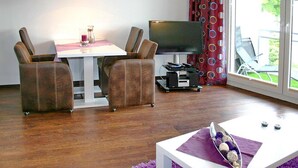 Una sala de estar moderna con comedor, televisor de pantalla plana y un gran ventanal con cortinas.