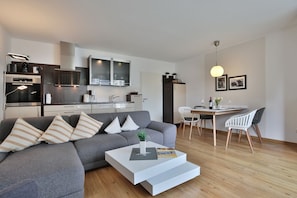 En moderne stue med en grå sofa, et hvidt sofabord og et spiseområde med et træbord og stole.