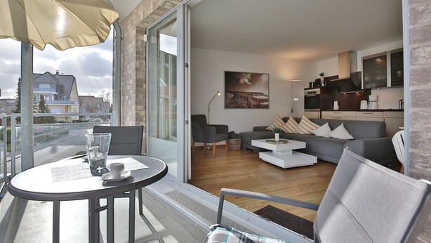 A modern living room with a grey sofa, a coffee table, and a dining table with chairs. There is a large window with a view of the city.