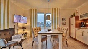 Una sala de estar moderna con comedor, paredes a rayas, un televisor de pantalla plana, un sofá, una mesa y una cocina con armarios y una cafetera.