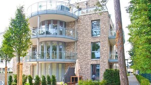 Un edificio residencial de varios pisos con balcones, un área de jardín y una escalera que lleva a la entrada.