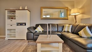 Una sala de estar con un sofá modular, un armario blanco, una mesa de centro de madera, una lámpara de pie y un espejo grande en la pared.