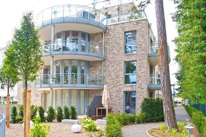 Un edificio residencial de varios pisos con balcones, un área de jardín y una escalera que lleva a la entrada.