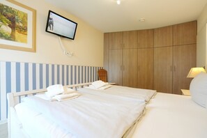 Habitación de hotel con dos camas, un televisor montado en la pared, un armario de madera y una lámpara en la mesita de noche.