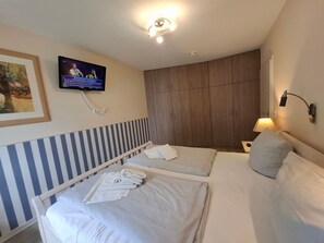 Habitación de hotel con dos camas, un televisor montado en la pared, una lámpara de noche y un cuadro enmarcado.