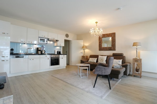 A modern kitchen with white cabinetry, a central island, and a dining area with a brown sofa and a grey armchair.
