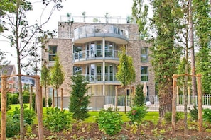 A multi-story residential building with a central courtyard, surrounded by trees and a metal fence.