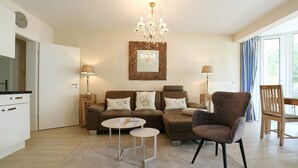 A living room with a sofa, armchair, coffee table, and a chandelier. - Home by the Sea Apartment 9 - Home by the Sea (Timmendorfer Strand)