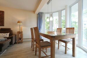 A modern living room with a glass dining table, wooden chairs, a sofa, and a lamp.