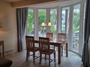 Ruokailutila, jossa on pöytä ja tuolit, suuret ikkunat verhoilla sekä näkymä vehreään maisemaan.