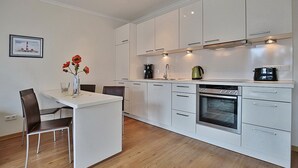 A modern kitchen with white cabinets, a built-in oven, and a dining area with a white table and chairs.