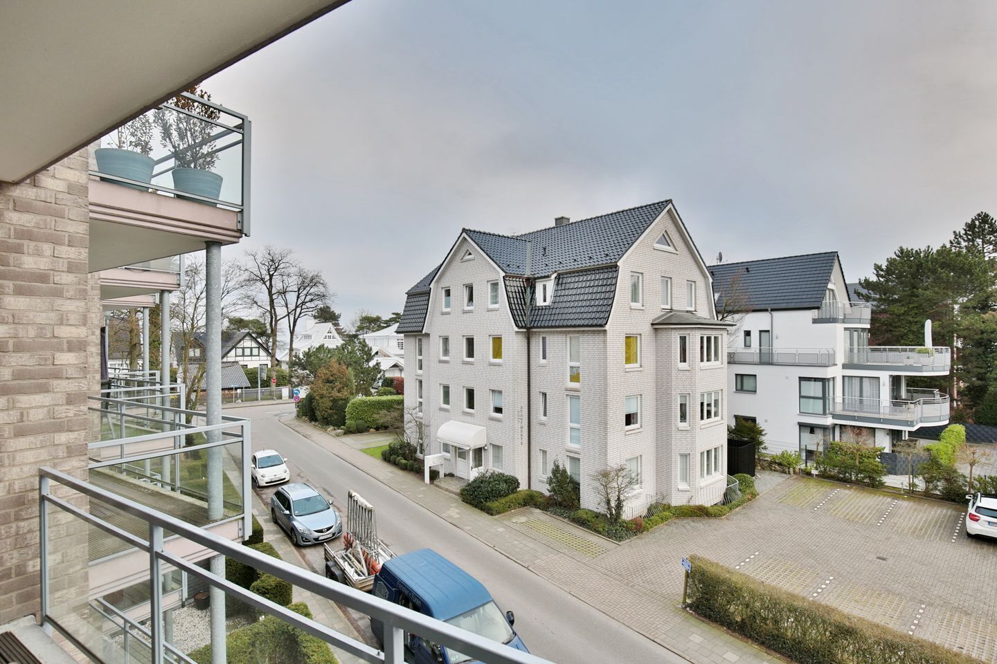 A modern residential building with a balcony, a driveway, and parked cars.