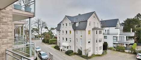 A modern residential building with a balcony, a driveway, and parked cars.