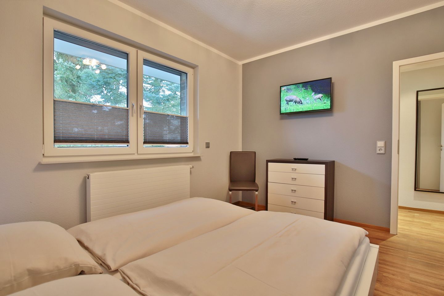 Een slaapkamer met een bed, een kaptafel, een stoel, een televisie en een raam met jaloezieën.