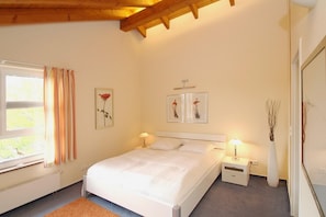 Une chambre à coucher avec un lit, des tables de chevet, une fenêtre avec des rideaux et des œuvres d’art murales.