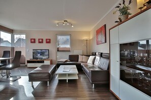 Un salon moderne comprenant un canapé, une table basse, un téléviseur et un coin repas avec des chaises et une table.
