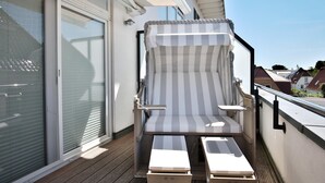A balcony with a striped chair and two side tables, a sliding glass door, and a view of houses. - Residenz Herrenbruchstraße 5 Apartment 8 - Residenz Herrenbruchstr. (Timmendorfer Strand)