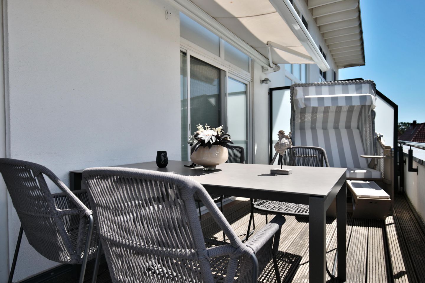 A balcony with a table, two chairs, a potted plant, and a striped awning.
