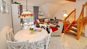 A cozy living room with a dining table, chairs, and a staircase.