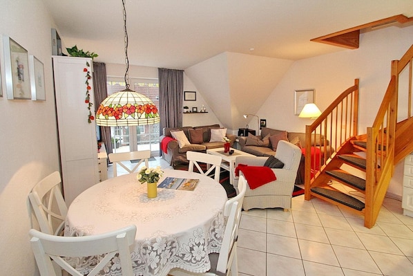 A cozy living room with a dining table, chairs, and a staircase.