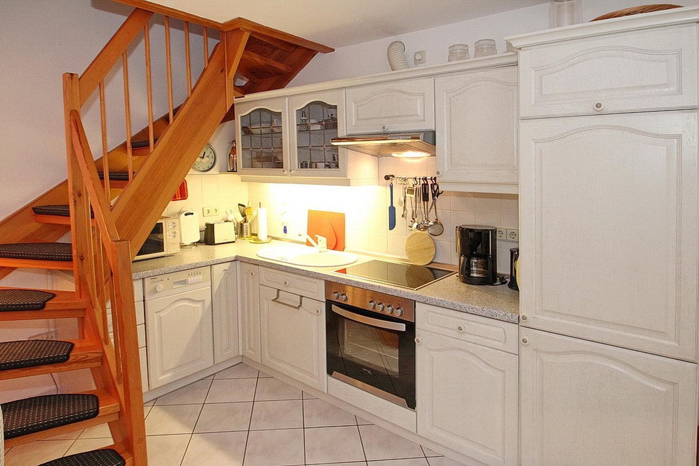 A kitchen with white cabinetry, a wooden staircase, a gas stove, and a coffee maker.