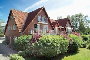 A two-story house with a sloped roof, a balcony with outdoor furniture, and a garden with various plants.