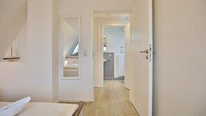 Un estrecho pasillo con techo inclinado que conduce a un dormitorio con tragaluz y una pequeña decoración de velero.