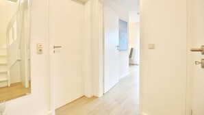 Un pasillo con puertas blancas, una escalera y un interruptor de luz en la pared.