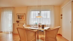 Ein Essbereich mit einem runden Tisch, Korbstühlen, einer Pendelleuchte und einem Bild an der Wand.