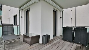 Ein Balkon mit Glastisch, Korbstühlen und einem Mülleimer.