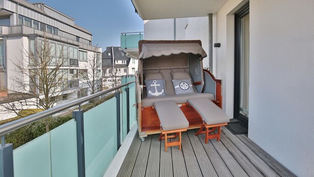 Ein Balkon mit Holzboden, einer gepolsterten Sitzecke mit Baldachin und Blick auf umliegende Gebäude.