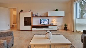 Una sala de estar moderna con un televisor de pantalla plana, una mesa de centro, un sofá y un mueble con puertas de vidrio.