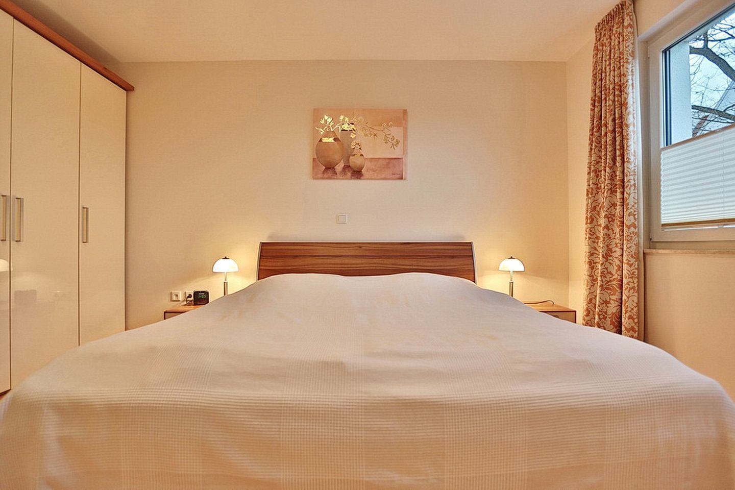 A hotel room with a large bed, two bedside lamps, a nightstand, and a window with curtains.